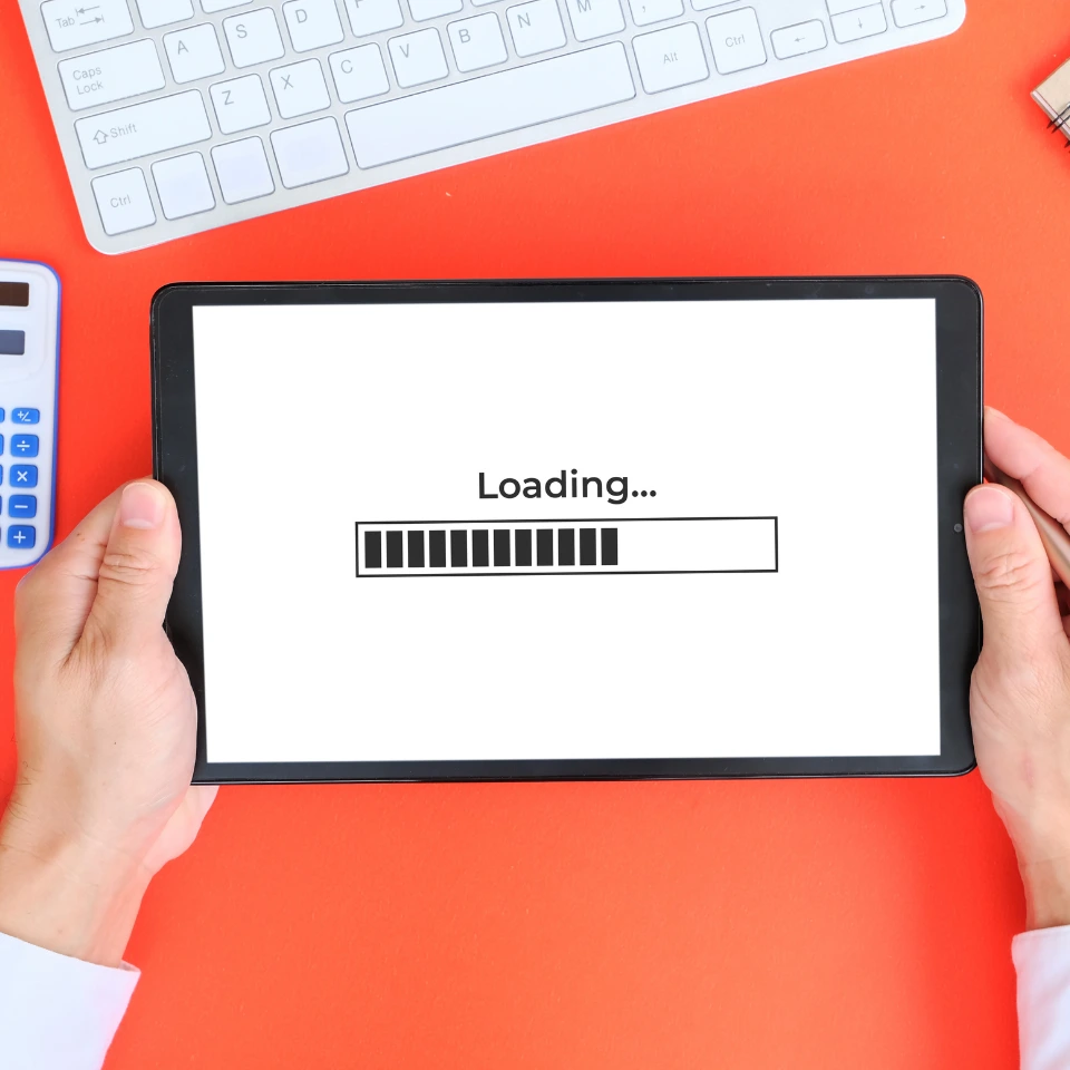 Person holding a tablet showing a loading screen with a progress bar, placed on a red desk near a keyboard and calculator