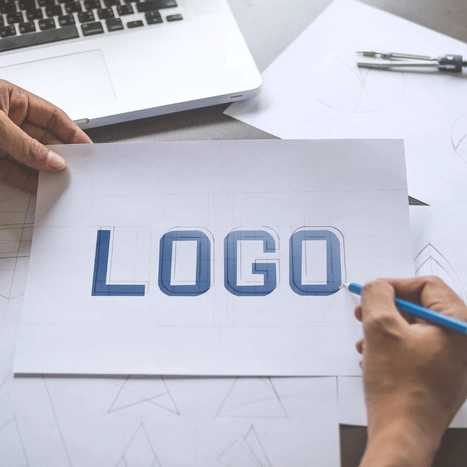 Designers sketching a logo concept with geometric guides and a laptop on the table