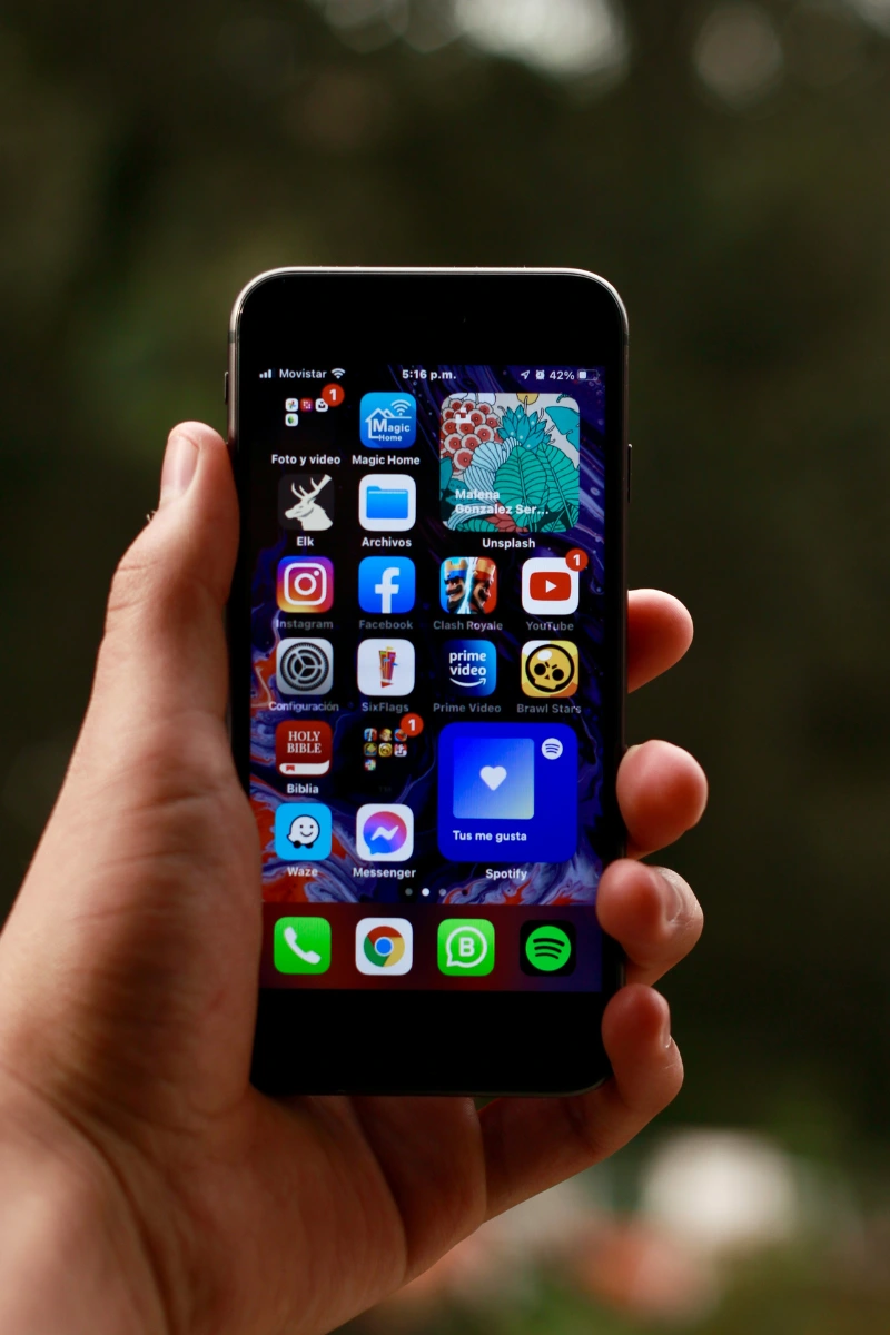 Person holding a smartphone showing the home screen with popular apps like Instagram, Facebook, YouTube, Prime Video, and Spotify