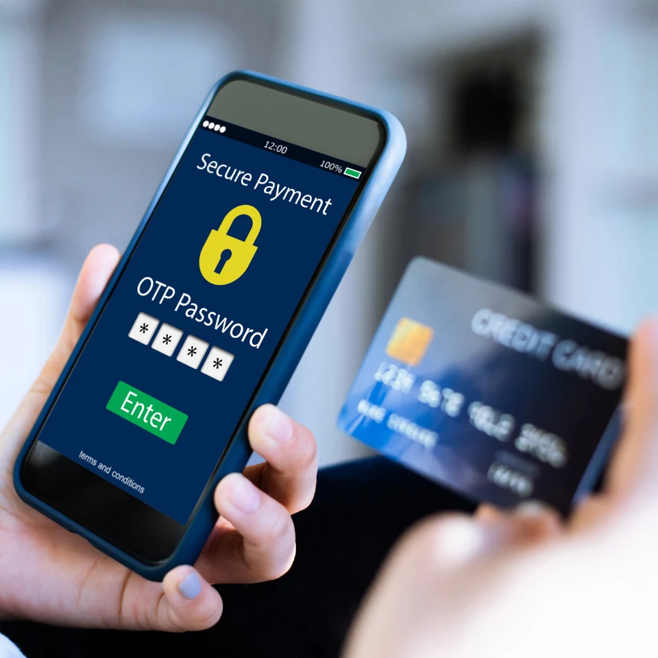 Person making a secure online payment using a smartphone with OTP verification screen and holding a credit card in the other hand.