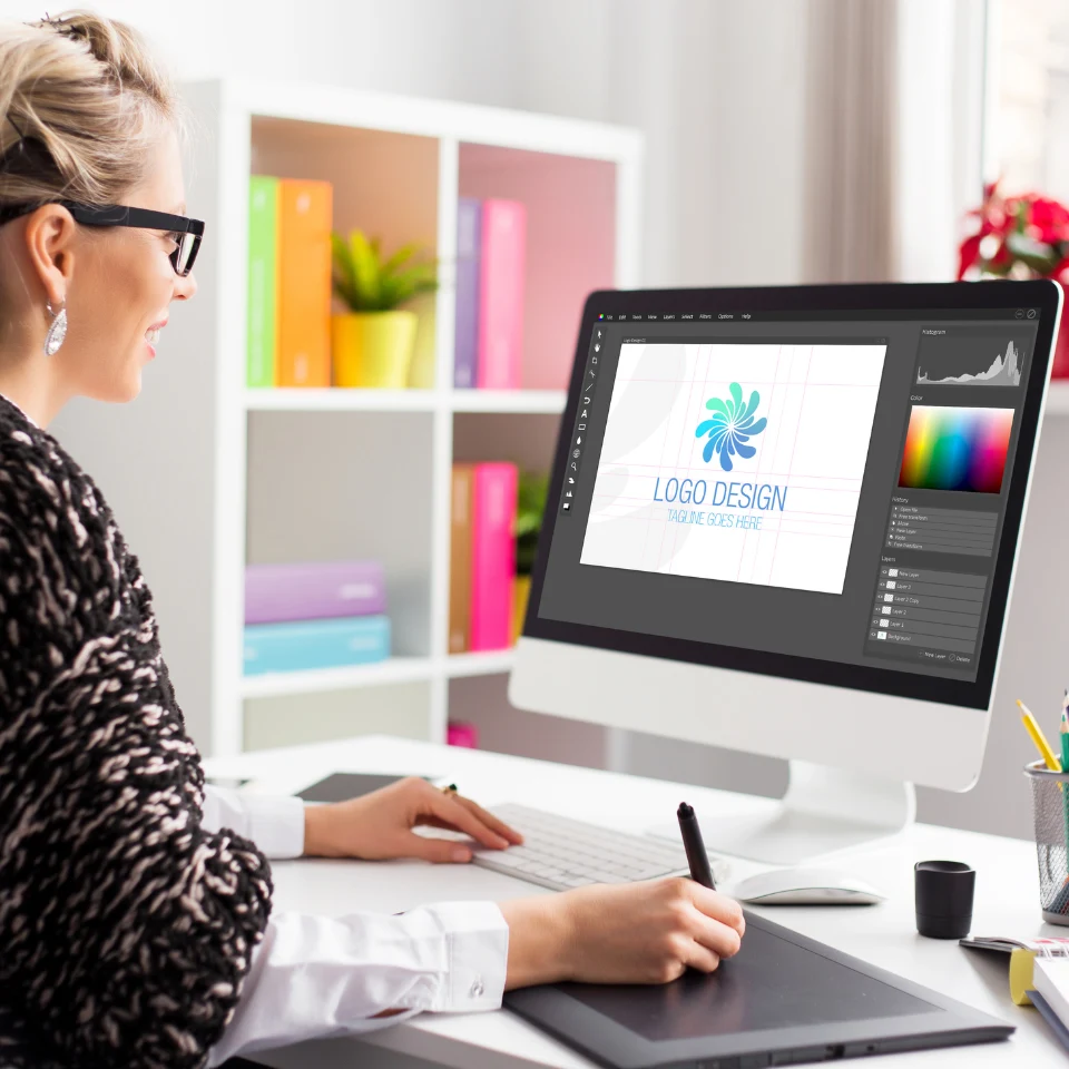 woman-with-glasses-using-drawing-tablet-to-design-colorful-logo-on-desktop-computer-in-bright-office