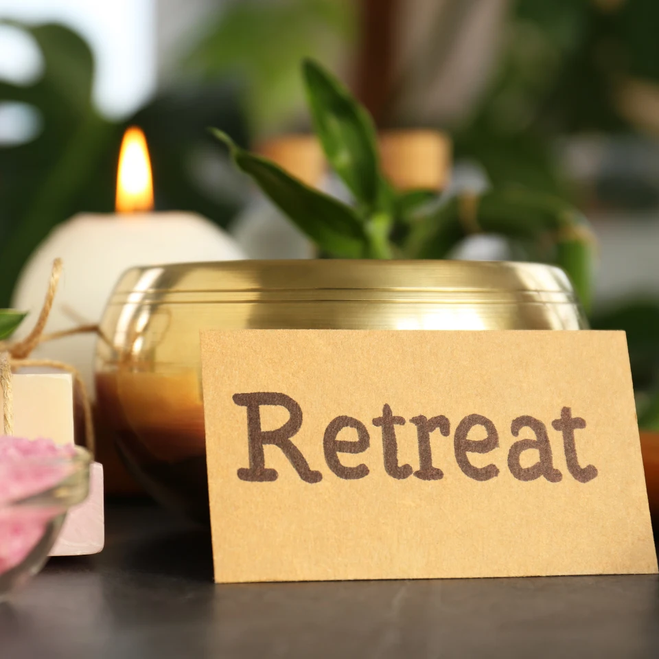 Spa setting with a lit candle, herbal bowl, pink bath salts, and a kraft paper card reading Retreat, creating a peaceful and relaxing ambiance.