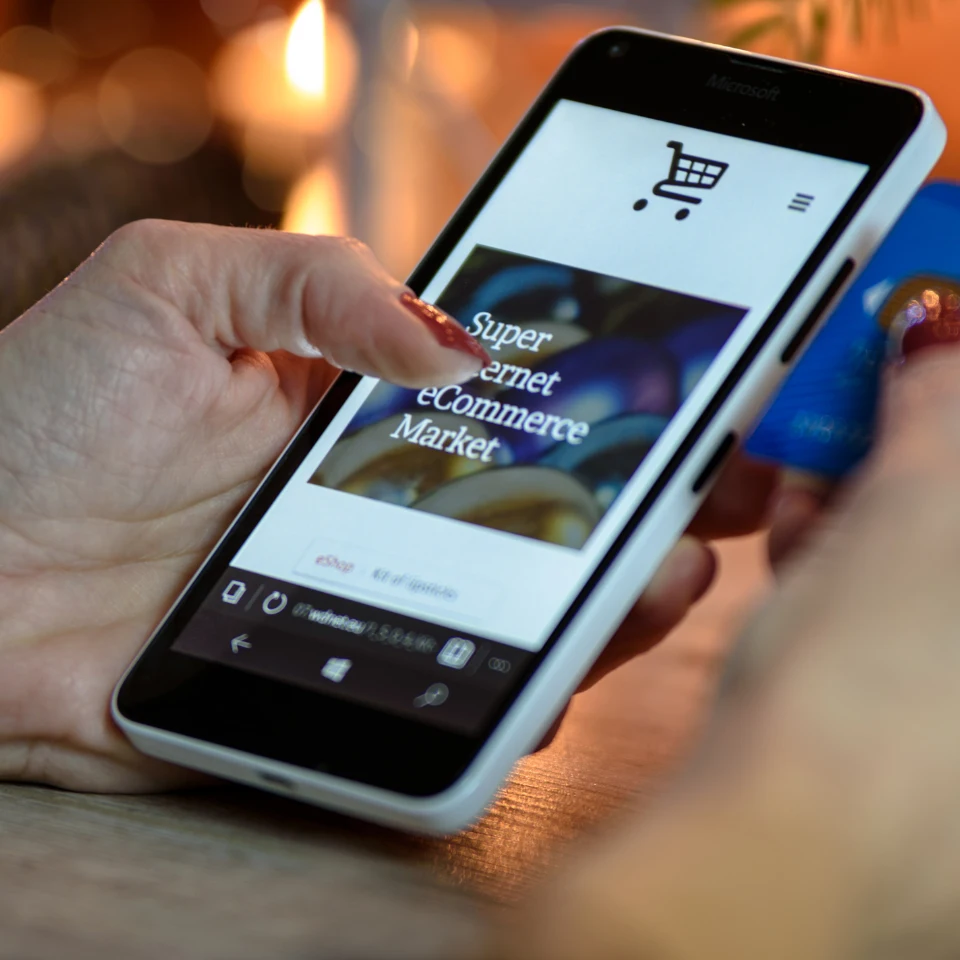 Hand holding smartphone displaying Super eCommerce Market shopping app with cart icon on screen in warm lighting.