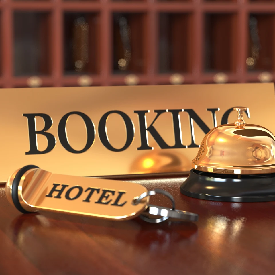 Close-up of a hotel reception desk with a golden service bell, a keychain labeled HOTEL, and a booking sign, with mail slots in the background.