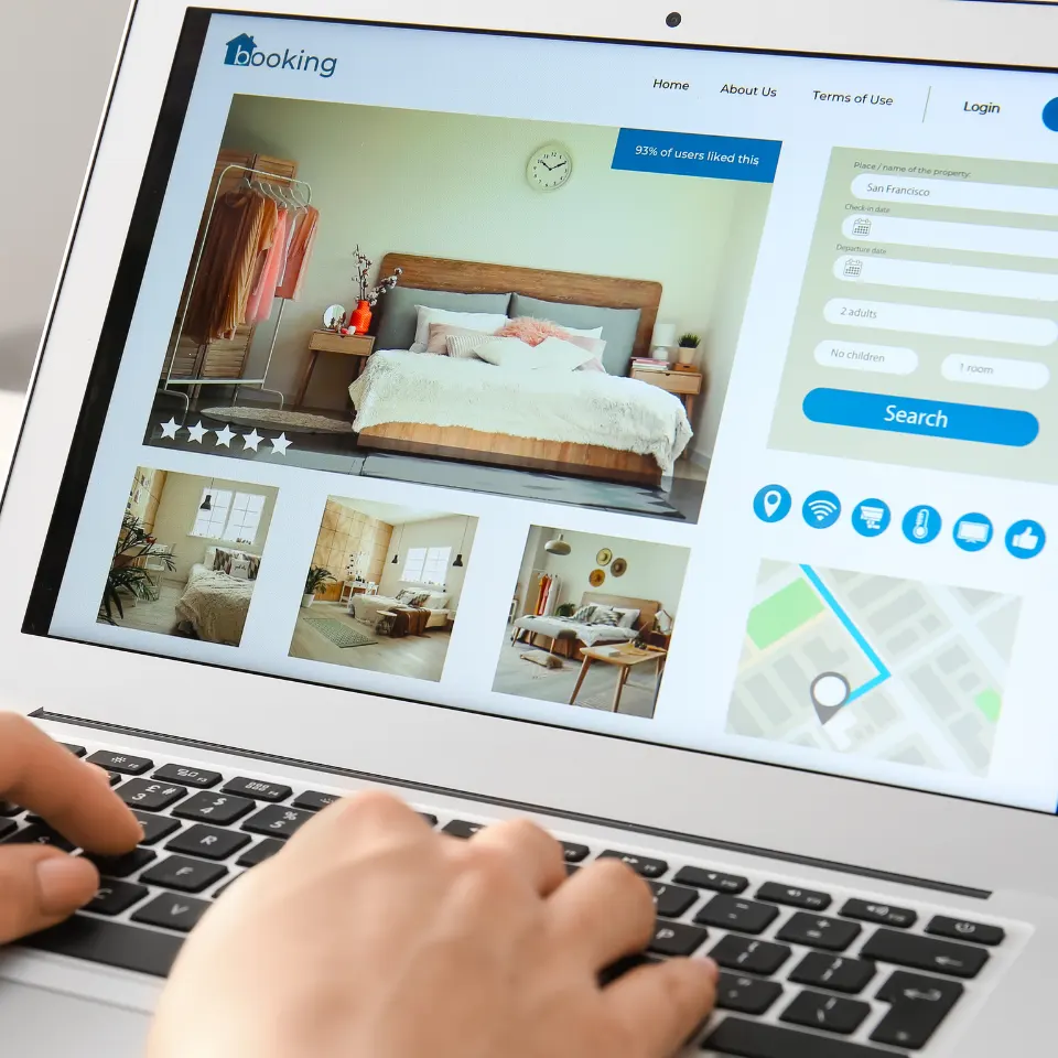 Close-up of a person browsing a hotel booking website on a laptop, displaying room images, search filters, and amenities icons for planning a stay.