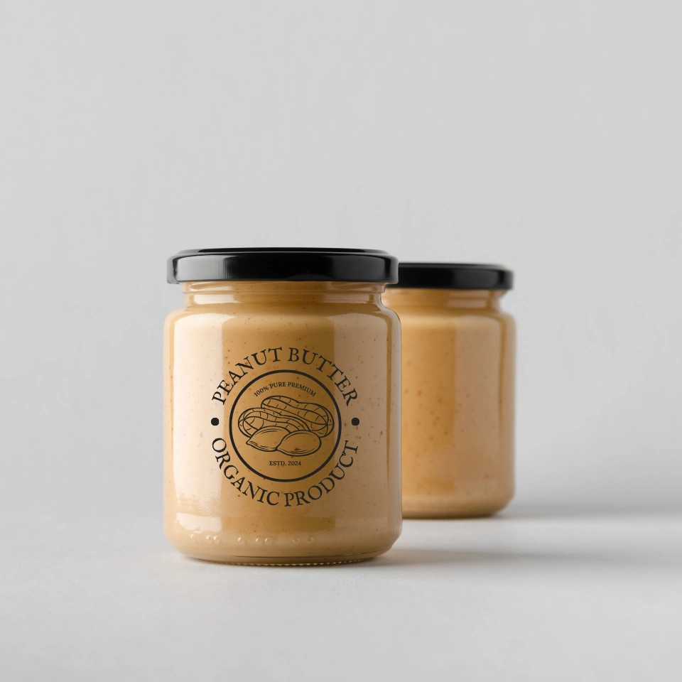 two-glass-jars-of-organic-peanut-butter-with-black-lids-and-vintage-style-labels-on-white-surface