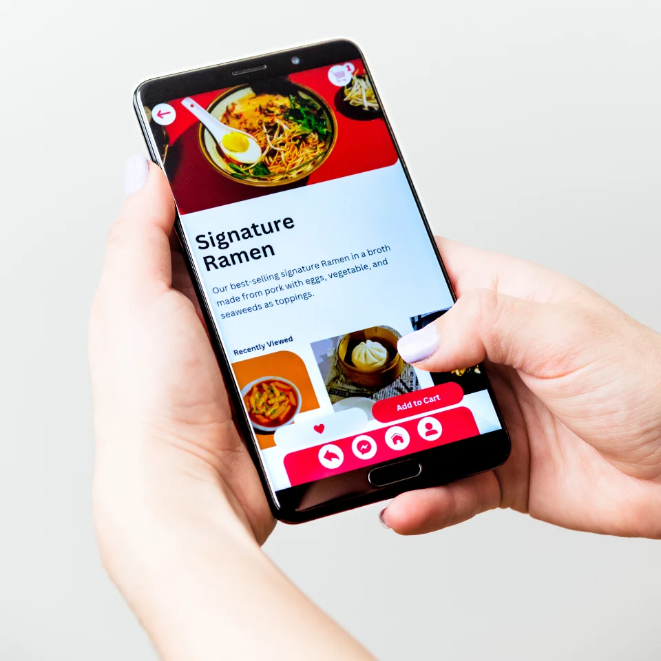 Person using a food delivery app on a smartphone, viewing a menu page for Signature Ramen with images and an 'Add to Cart' button