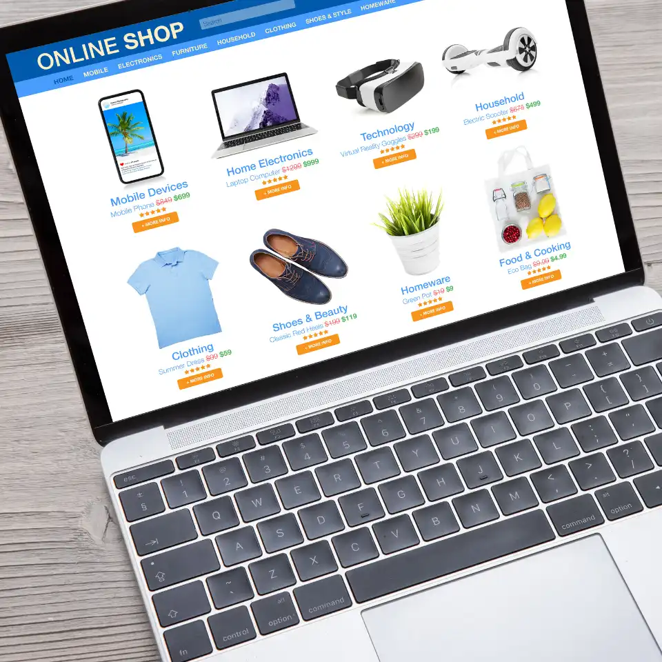 Laptop displaying an online shop homepage with categories like electronics, clothing, homeware, and food on a wooden surface.