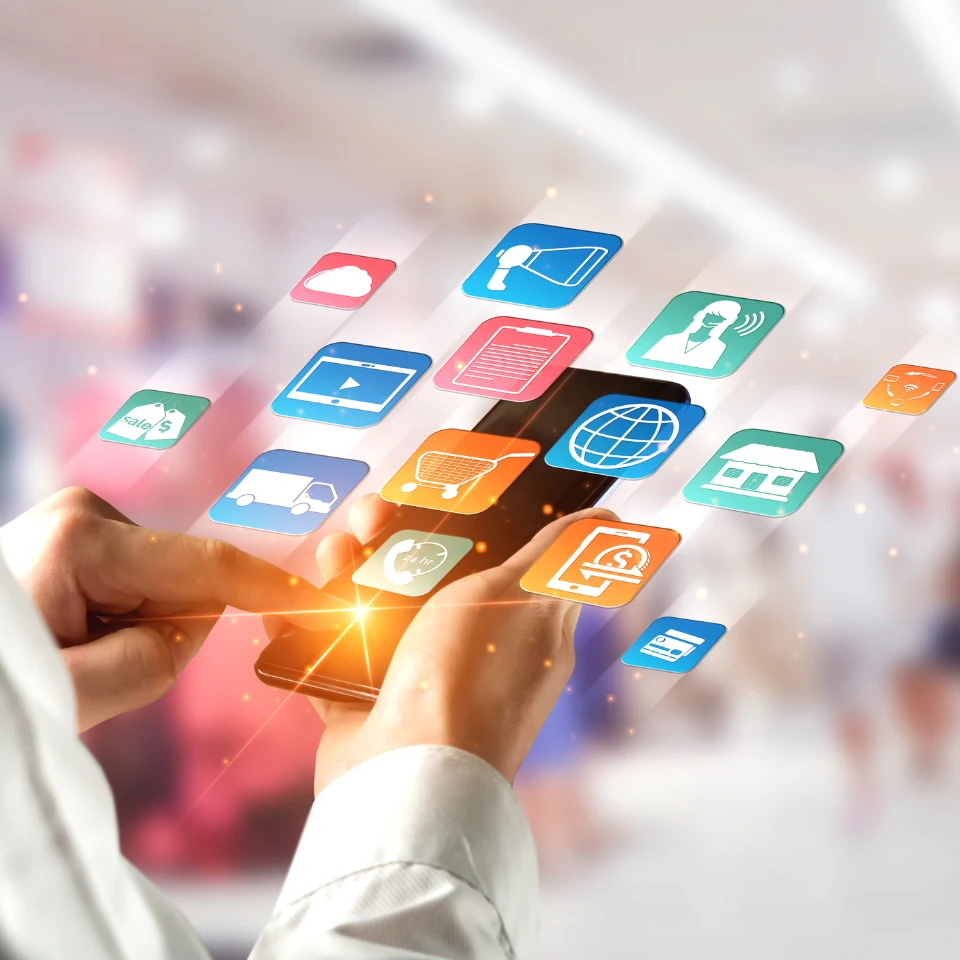 Person using a smartphone with colorful digital app icons floating above the screen, representing various online services and social media in a blurred background.