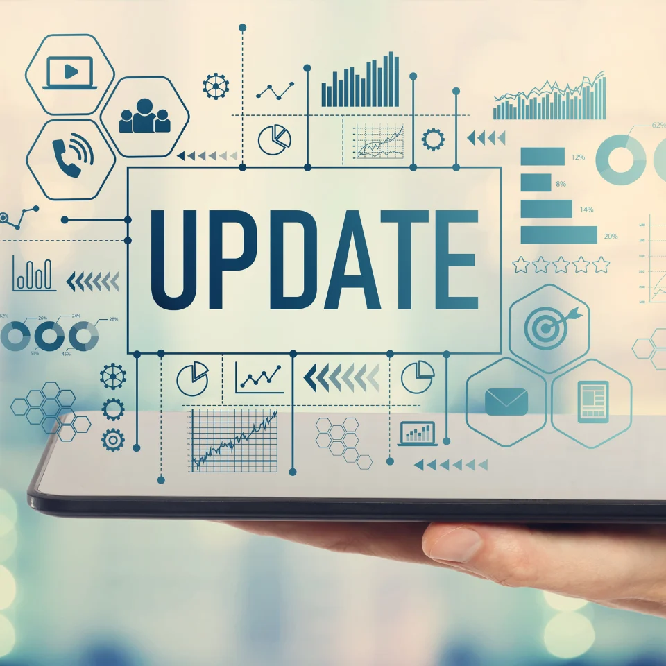 Hand holding a tablet displaying the word UPDATE surrounded by digital graphs, charts, icons, and technology interface elements.