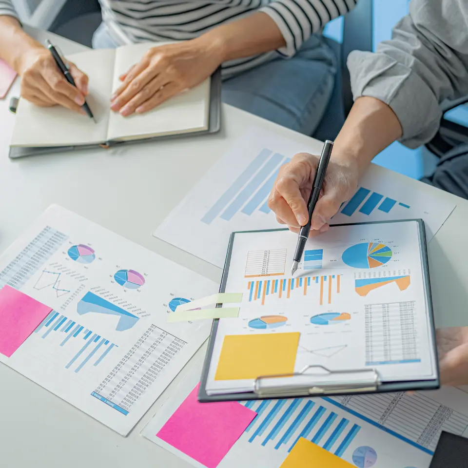 Two people analyzing marketing data and charts with bar graphs, pie charts, and notes during a business meeting