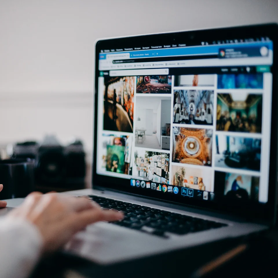 Person browsing a gallery of interior design and art images on a laptop, with hand on keyboard and camera in the background.