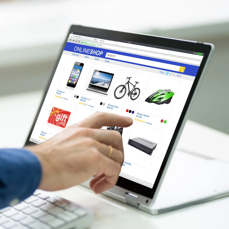 Person browsing online shop website on laptop, pointing at products including phone, laptop, bicycle, and gift card items.