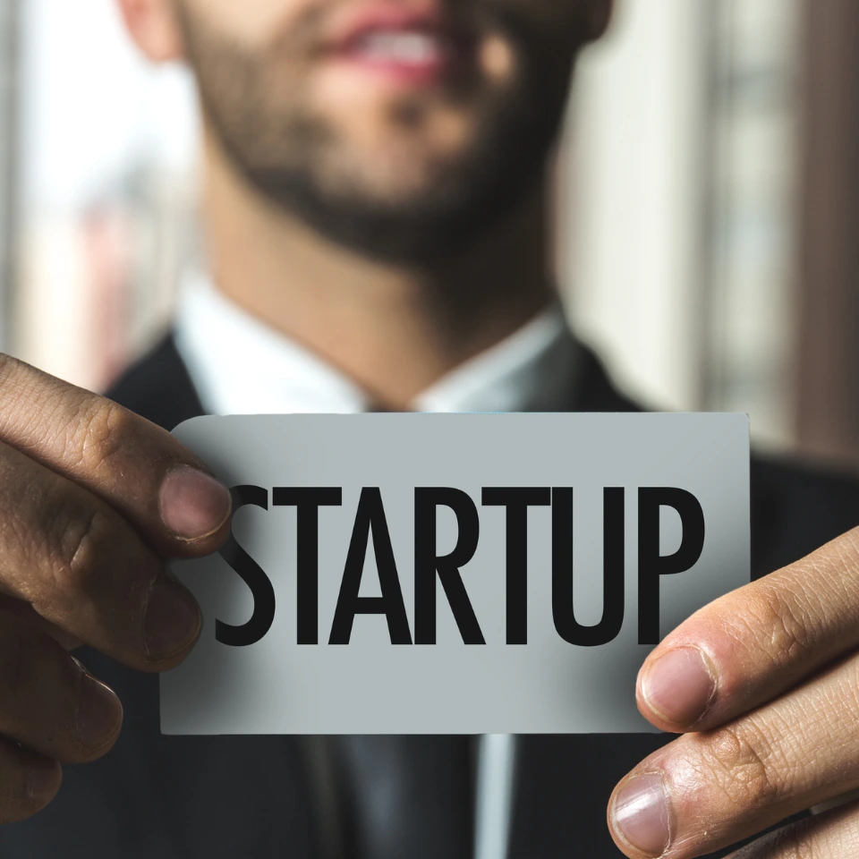 Smiling businessman holding transparent card with STARTUP text, representing entrepreneurship and new business ventures.