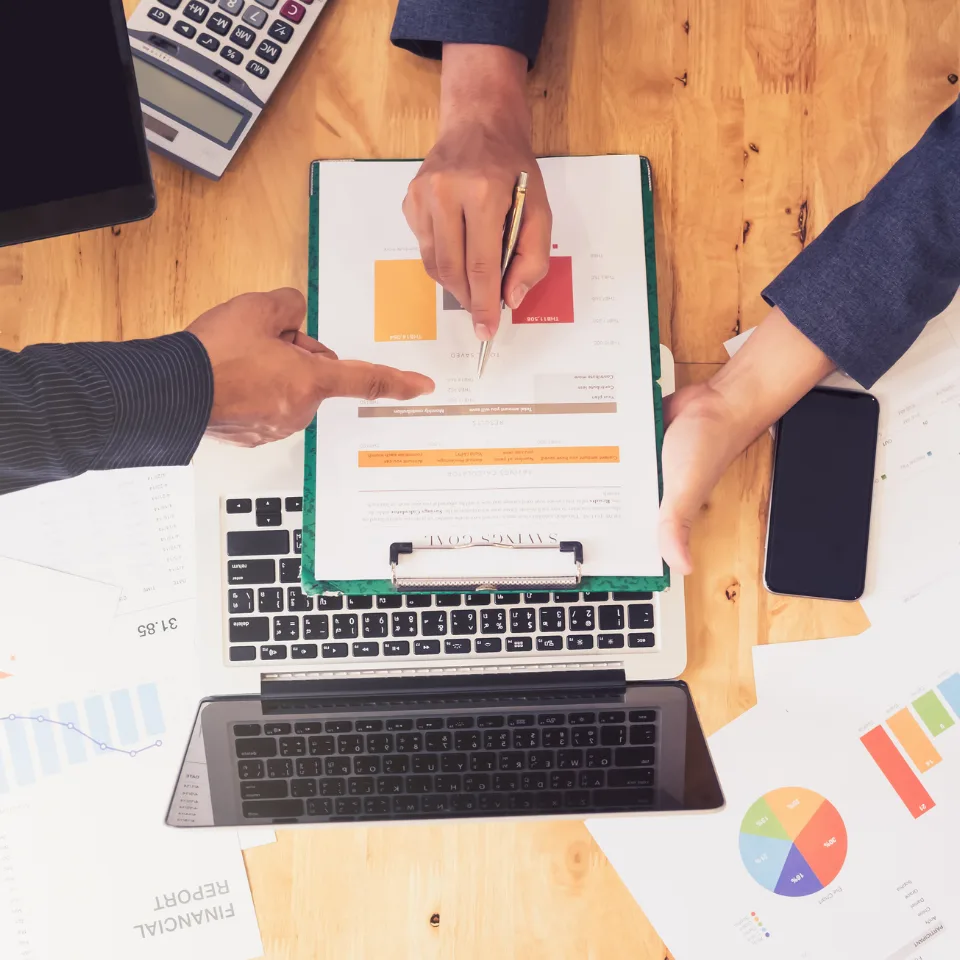 Business team analyzing charts and graphs on wooden desk with laptops, calculator, and colorful data visualization materials.
