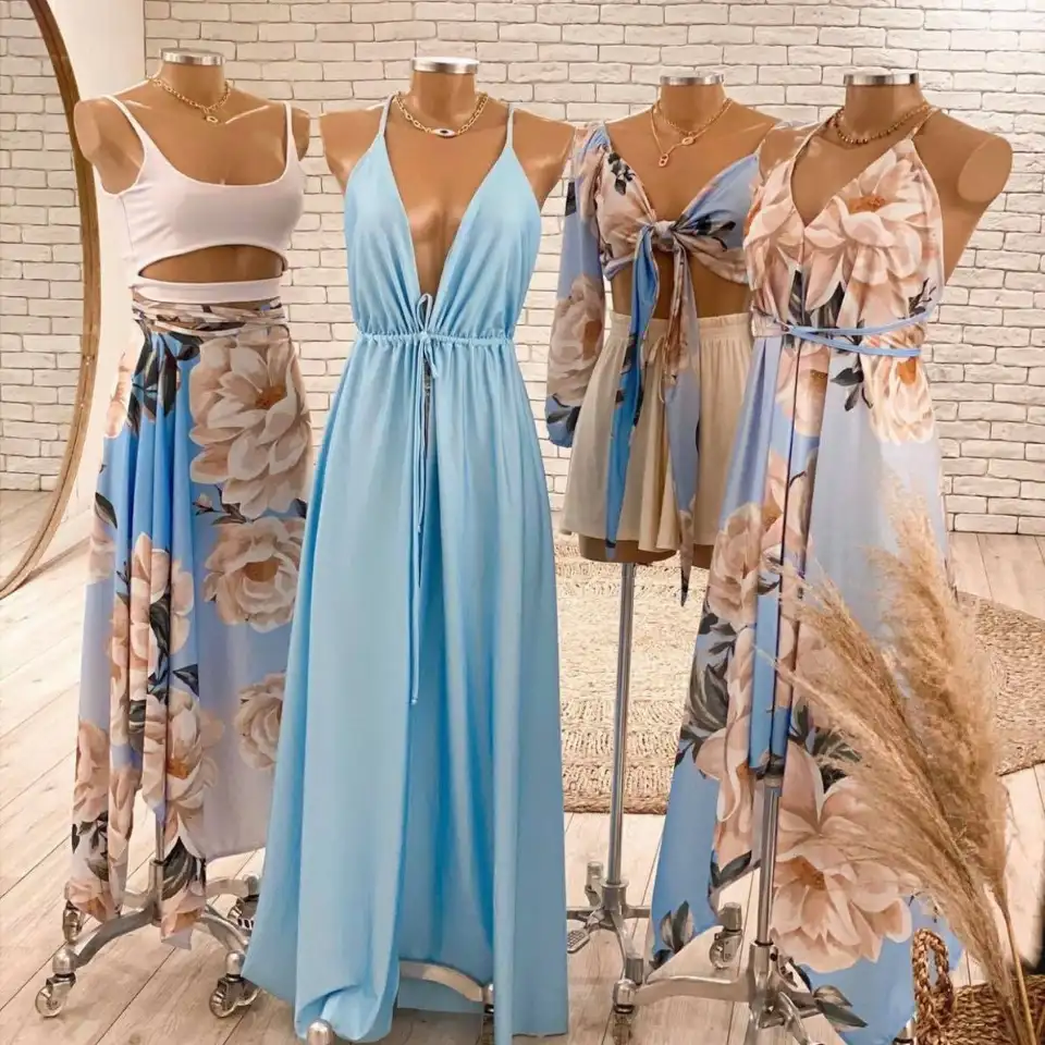 Four mannequins displaying coordinated women's outfits in soft blue tones with large floral prints, including maxi dresses, crop tops, and flowy skirts, set in a stylish boutique with a light brick wall background.